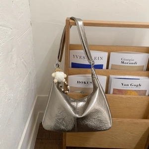 Detalle de bolso hobo plateado con textura plisada y colgante de peluche blanco