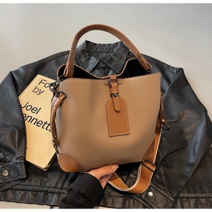 Detailed view of brown lychee texture bucket bag with striped strap and vintage book