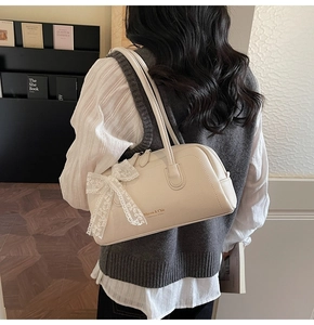 Détail du sac en cuir crème avec un nœud en dentelle et logo doré élégant