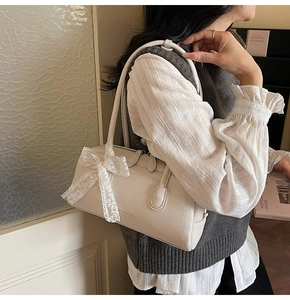 Détail du sac Boston en cuir crème avec logo doré et nœud en dentelle sur l'anse