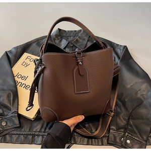 Detail of dark brown pebble leather bucket bag with contrast white stitching and wide strap
