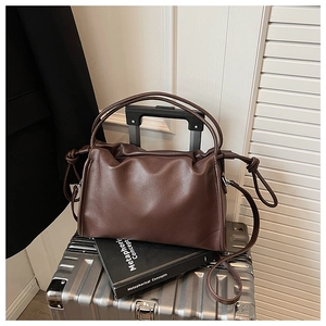 Détail du sac nuage plissé marron foncé en cuir souple posé sur une valise en métal