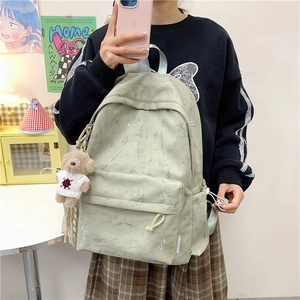 Detail of light green student backpack with marble texture and plush bear charm