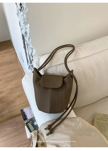 Detail of dark brown leather bucket bag with vertical stitching on white sofa