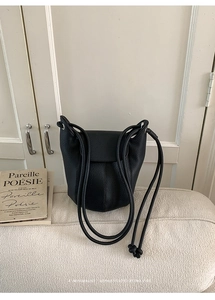 Close-up of black lychee grain leather bucket bag with knotted shoulder strap detail