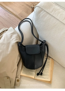 Detail of black pebbled leather pumpkin bucket bag with flap and long strap on a sofa