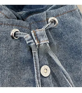 Détail macro du sac à dos en jean bleu montrant les coutures orange et la boucle métallique