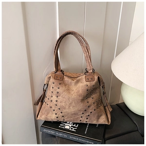 Détail d'un sac cabas marron vintage avec clous métalliques sous une lumière chaude