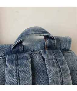 Gros plan de la poignée supérieure et des bretelles renforcées du sac à dos en denim
