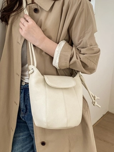 Chic cream-colored pumpkin shoulder bag in lychee texture worn by a model in a trench coat