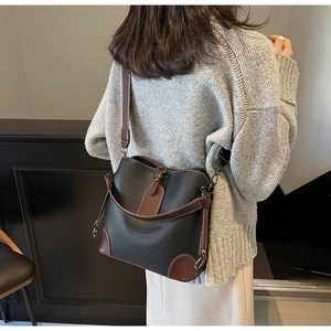 Detail of a black pebbled leather bucket bag with brown trim on a textured knit sweater