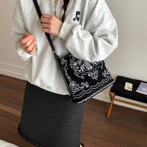 Détail du sac seau vintage en toile avec broderie florale blanche et bandoulière en cuir