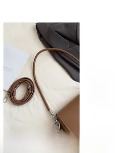 Détail d'un sac à main en cuir marron avec boucles métalliques et deux bandoulières