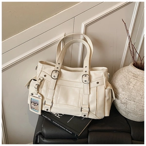 Dettaglio della borsa tote in pelle color crema con fibbie e ciondolo a forma di orso