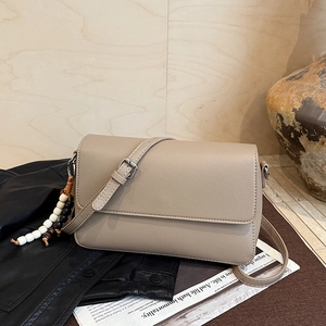Détail d'un sac en cuir beige avec porte-clés perlé posé sur un magazine