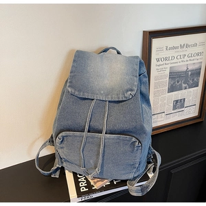 Detail of light blue denim backpack with front zipper pocket and buckle flap closure