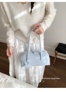 Close-up of light blue leather handbag featuring a star charm and elongated dual handles