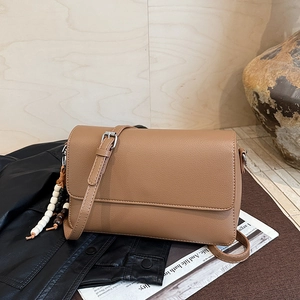 Détail du sac en cuir marron à motif litchi avec breloque perlée sur une veste en cuir noir