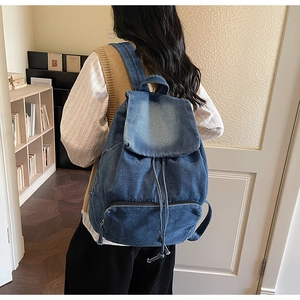 Detail of blue washed denim backpack with drawstring flap and front zipper pocket