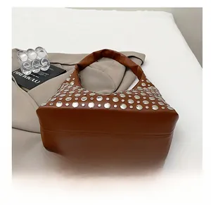 Dettaglio dei rivetti in argento su una borsa a secchiello vintage in finta pelle marrone