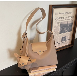 Minimalist beige leather shoulder bag with matching mini charm on a stylish wide strap