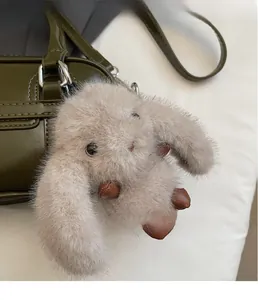 Détail d'un pendentif lapin en peluche beige avec touches de cuir marron sur un sac vert