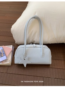 Detail of light blue baguette bag with long handles and a star pendant on a wooden floor