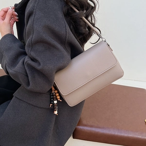 Détail du sac à rabat en cuir grainé taupe avec breloque en bois sur un mannequin
