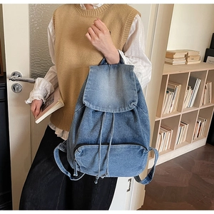 Blue denim backpack detail with drawstring closure and front pocket in a library setting