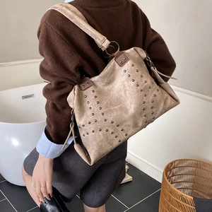 Détail d'un grand sac cabas beige avec rivets métalliques et anse marron foncé