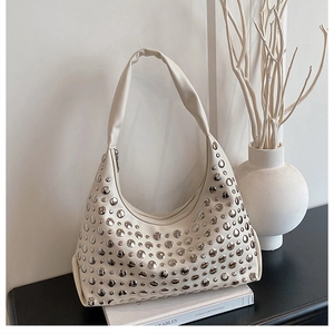 Detail einer weißen Hobo-Tasche mit silbernen Nieten auf einem Buch in minimalistischem Design