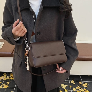 Sac bandoulière marron foncé en cuir grainé avec pendentif perlé porté par un modèle