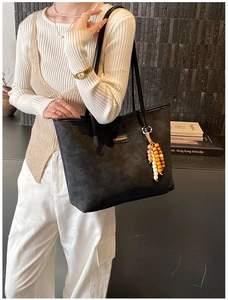 Close-up of black tote bag featuring geometric embossed pattern and wooden bead charm