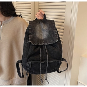 Detail of black washed denim backpack with drawstring closure and vintage metal hardware