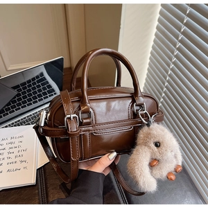 Close-up of retro brown handbag with a cute beige bunny charm and metal buckle detail