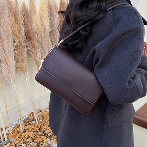 Détail du sac à rabat en cuir marron foncé porté par un mannequin dans un décor d'automne
