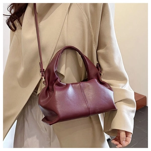 Detail of burgundy cloud-shaped handbag featuring soft pleats and shoulder strap on trench coat