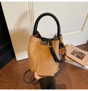 Détail du sac seau en daim camel avec poignée en cuir noir et breloque florale vintage