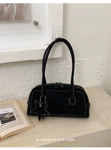 Detail of black suede shoulder bag featuring white contrast stitching and a star charm