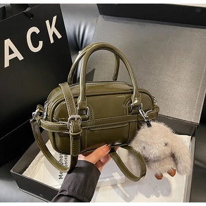 Detailed view of olive green patent leather handbag with plush bunny charm in gift box