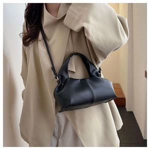 Detail of a black ruched faux leather crossbody bag worn over a beige oversized blazer
