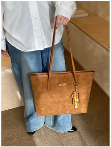 Brown suede tote bag with Carolmanti logo and wooden bead charm detail held by model