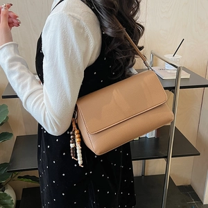 Détail du sac en cuir camel avec un pendentif élégant en perles de bois et finitions argentées