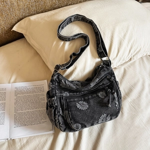 Close-up of black denim crossbody bag with white daisy floral patterns and vintage zippers