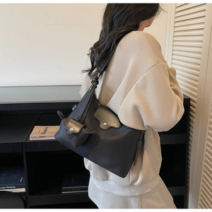 Detail of minimalist black shoulder bag with textured leather flap and round silver buckle