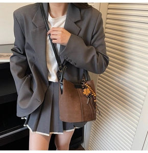 Détail du sac seau en daim marron foncé avec poignées en cuir et breloque trèfle à quatre