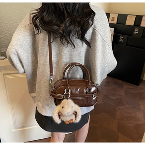 Detail of dark brown leather handbag featuring a plush bunny charm and belt buckle decor