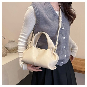 Close-up of a cream-colored soft leather cloud bag worn by a model in a minimalist setting