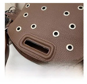 Dettaglio borsa in pelle marrone con occhielli metallici e cuciture rifinite a mano