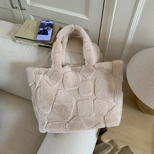 Detail of beige plush tote bag with embossed geometric patterns on a cozy sofa